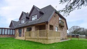 A two-story house with a stone facade, a wooden deck, and a sloped roof. - Cwm Gran Meadows (Pontyclun)