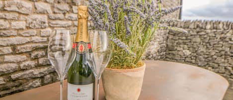 A bottle of champagne and two glasses on a table with a potted lavender plant.