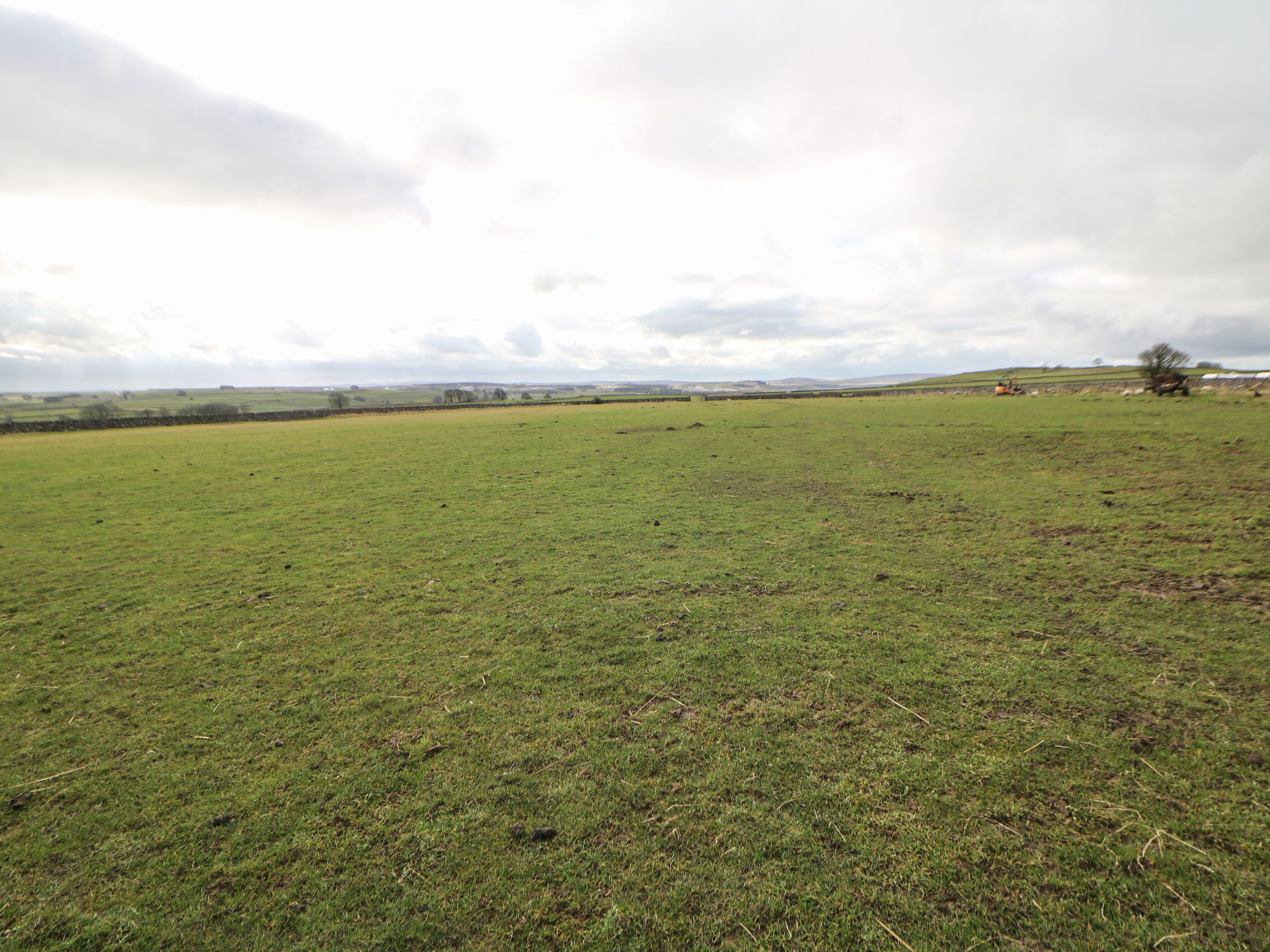 A wide, open field with a distant view of rolling hills and a cloudy sky.
