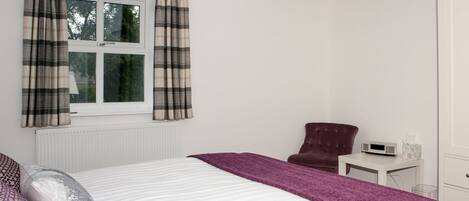 A bedroom with a bed, a chair, a bedside table, and a window with curtains.
