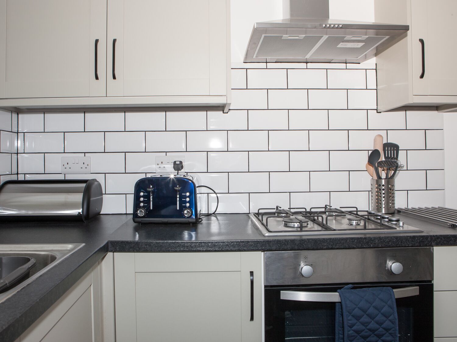 A modern kitchen with white cabinets, a gas stove, a toaster, and a sink.