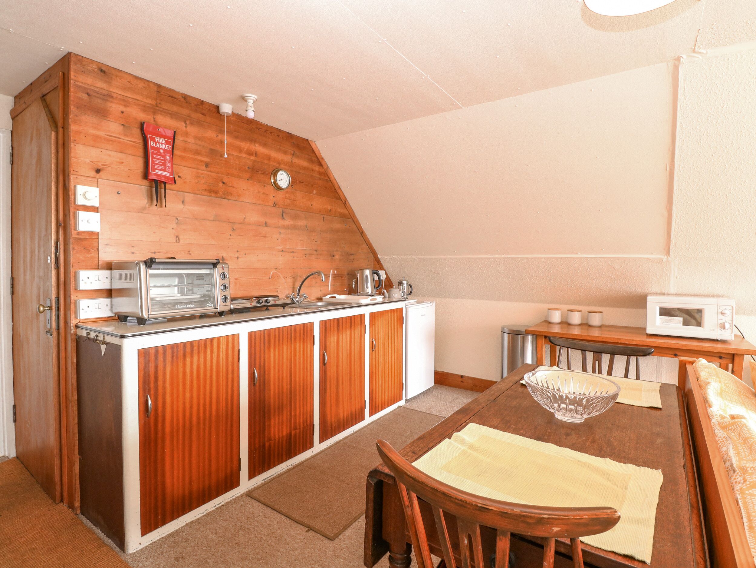 A compact kitchen with wooden cabinets, a built-in toaster, a sink, and a microwave.