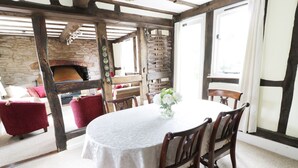 Een eethoek met een ronde tafel, houten stoelen en een witte tafelkleed. Achtergrond is een stenen muur en een open haard.