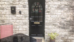 A stone building with a black door, a mailbox, and a potted plant. - 1A Market Square (Buxton)