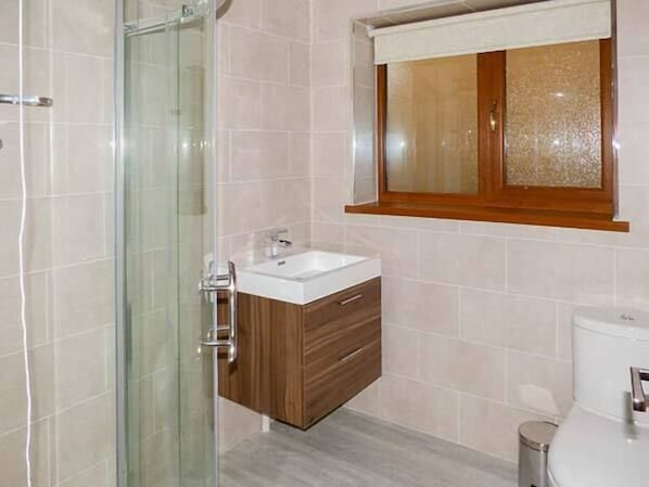 Une salle de bain avec une douche à parois de verre, un meuble-lavabo en bois et des toilettes.