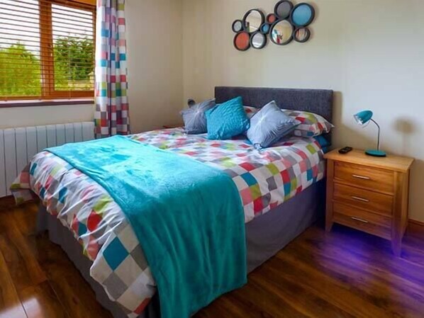 Un dormitorio con cama, mesita de noche, un reloj de pared y una ventana con persianas.