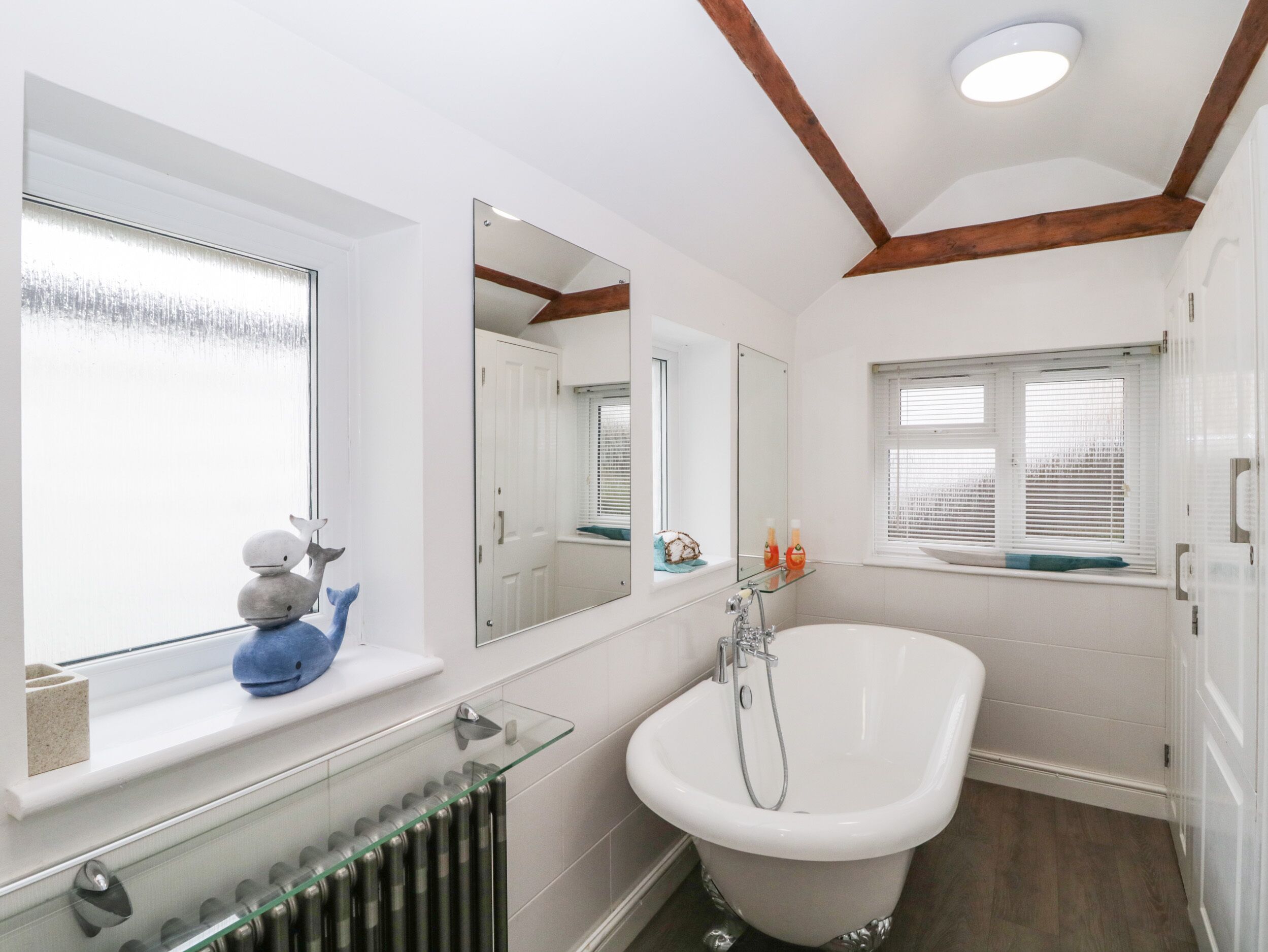A bathroom with a bathtub, a window with a view, a radiator, and a mirror.