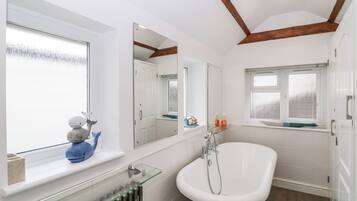 A bathroom with a bathtub, a window with a view, a radiator, and a mirror.