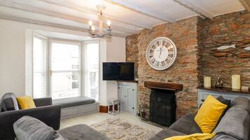 A living room with a stone wall, a fireplace, a large clock, and a television.