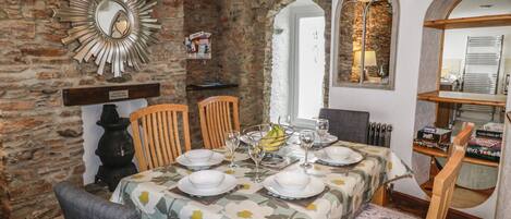 A dining area with a stone wall, wooden beams, and a mirror. There are tables set with plates, glasses, and a fruit bowl.