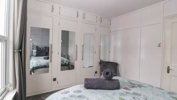 Un dormitorio con cama, armario, espejo y ventana con cortinas.