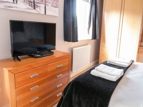 A hotel room with a wooden dresser, a flat-screen TV, a bed with a black and white blanket, and a window with black curtains. - 9 Navigation Square (Skipton)