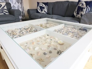 A living room with a glass-top coffee table displaying various seashells and starfish. - Bungalow (Fishguard)