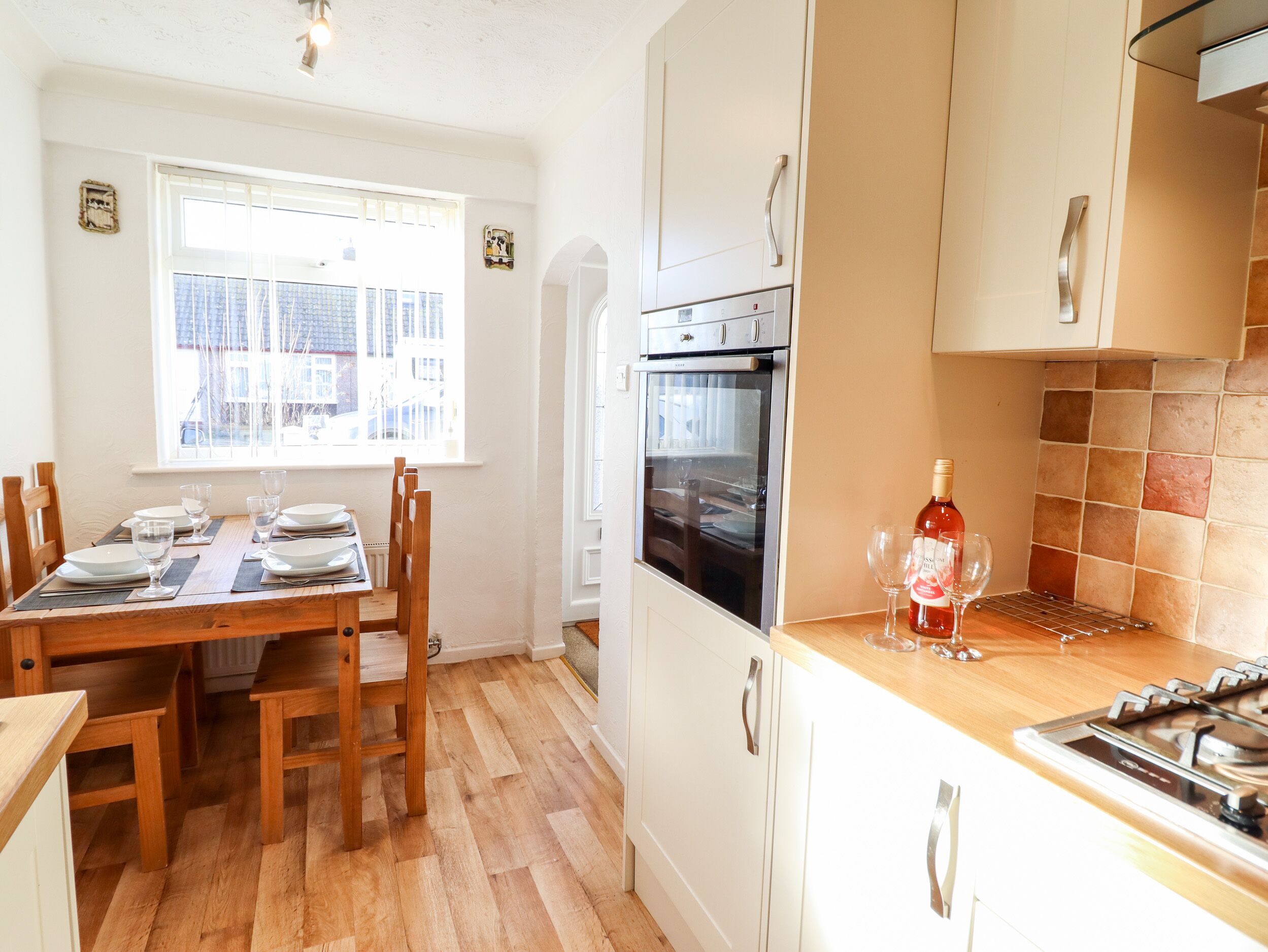 A kitchen with wooden flooring, white cabinets, a built-in oven, and a dining table set for four.