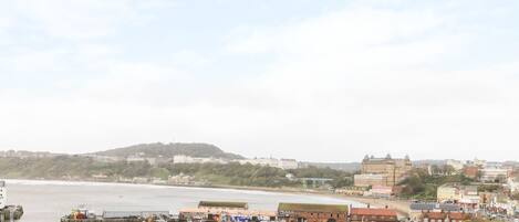 A coastal town with historic buildings, a harbor with boats, and a hill in the background.