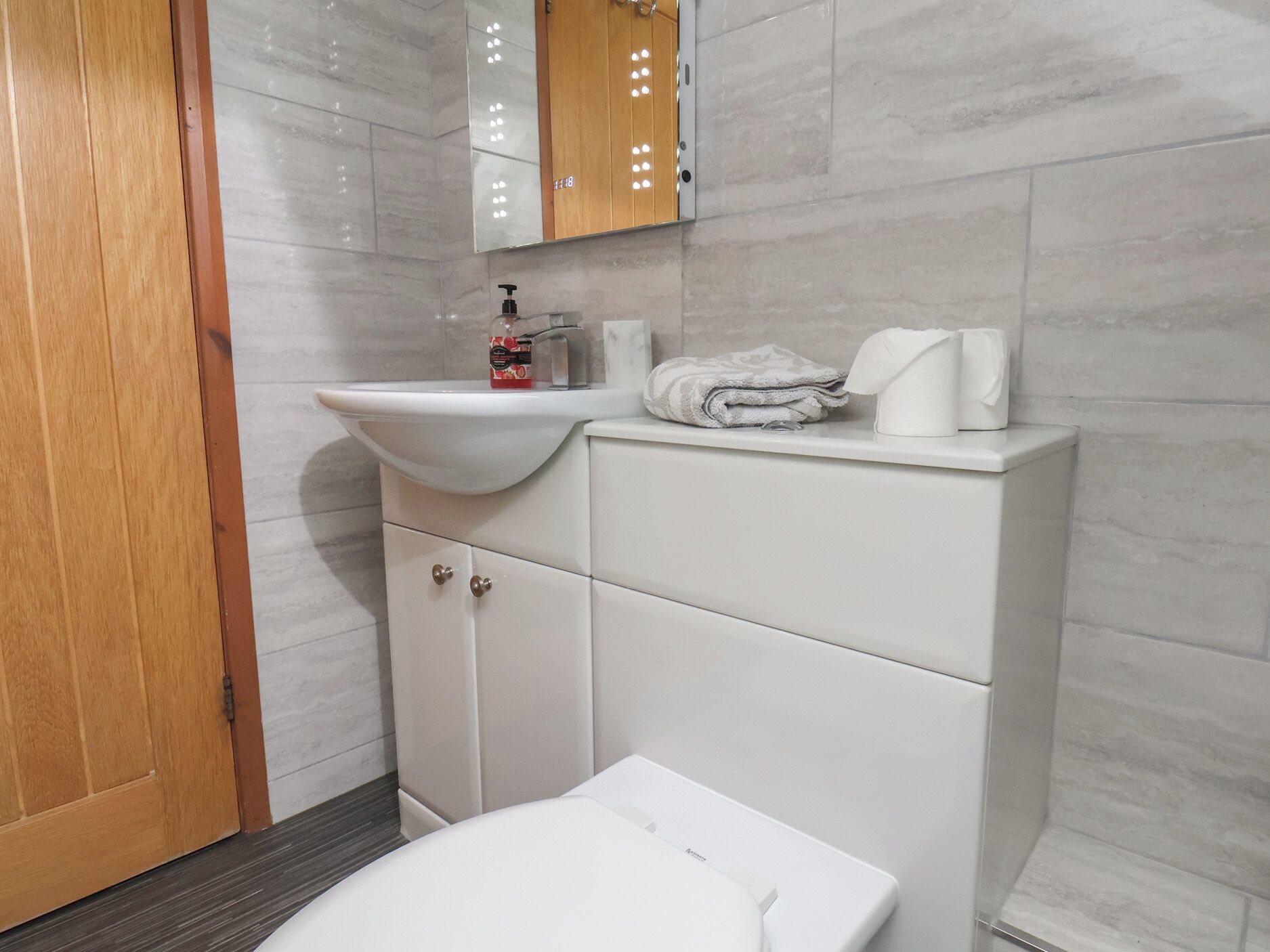 A bathroom with a white sink, a mirror, a wooden door, and a toilet.