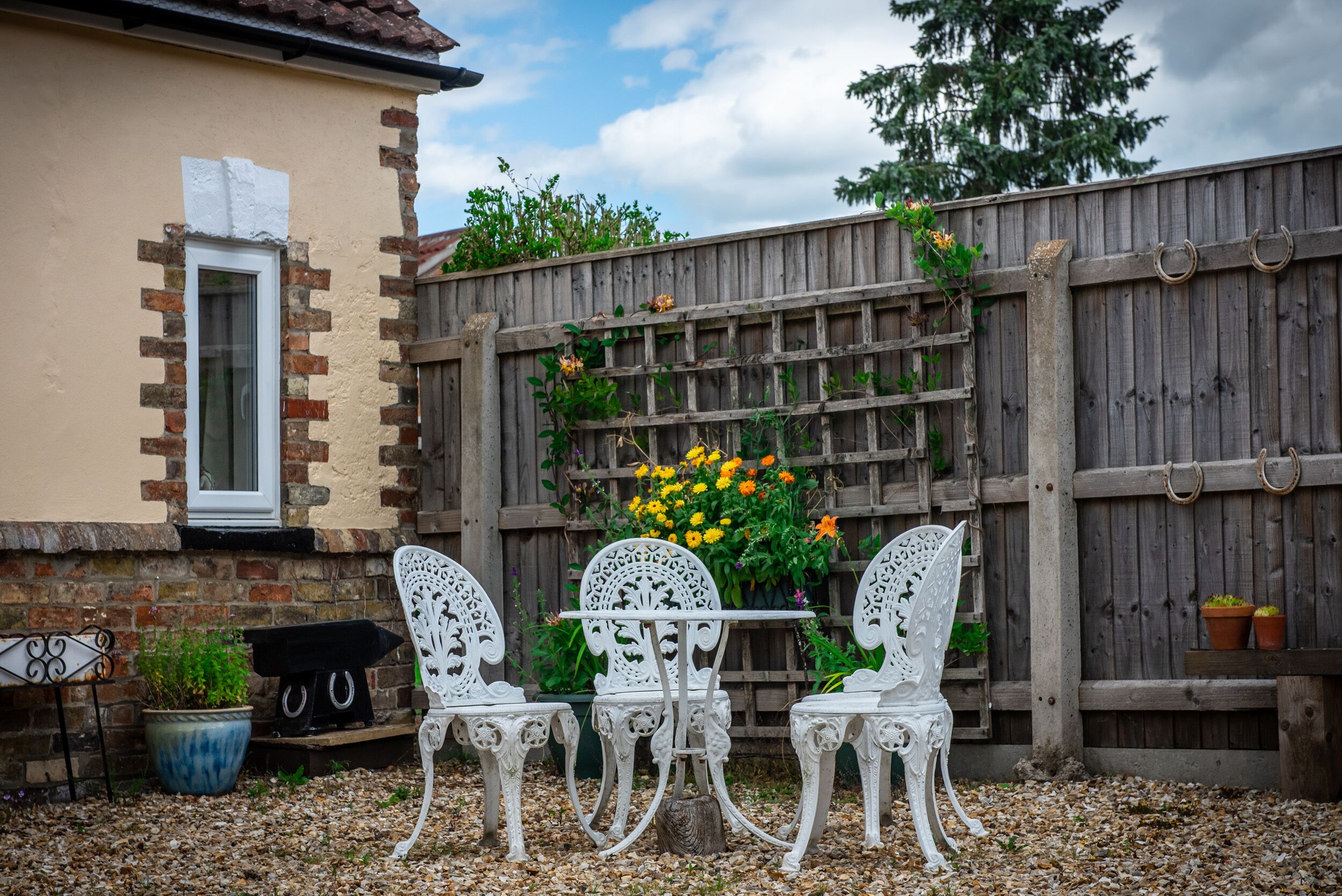 Une terrasse avec une table et des chaises, une clôture en bois et un pot de fleurs.