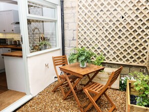 Une petite terrasse avec une table et des chaises en bois, un pot de fleurs et un mur en treillis.