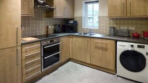 A kitchen with wooden cabinets, a double oven, a microwave, a sink, and a washing machine. - Jay's Nest (Hope Valley)