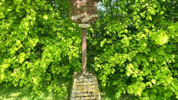 A stone sign with "GREAT CARLTON" and "MILLENNIUM 2000" engraved on it, mounted on a brick base, surrounded by lush green foliage.