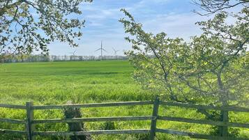A rural landscape with a wooden fence, green fields, and wind turbines in the distance.