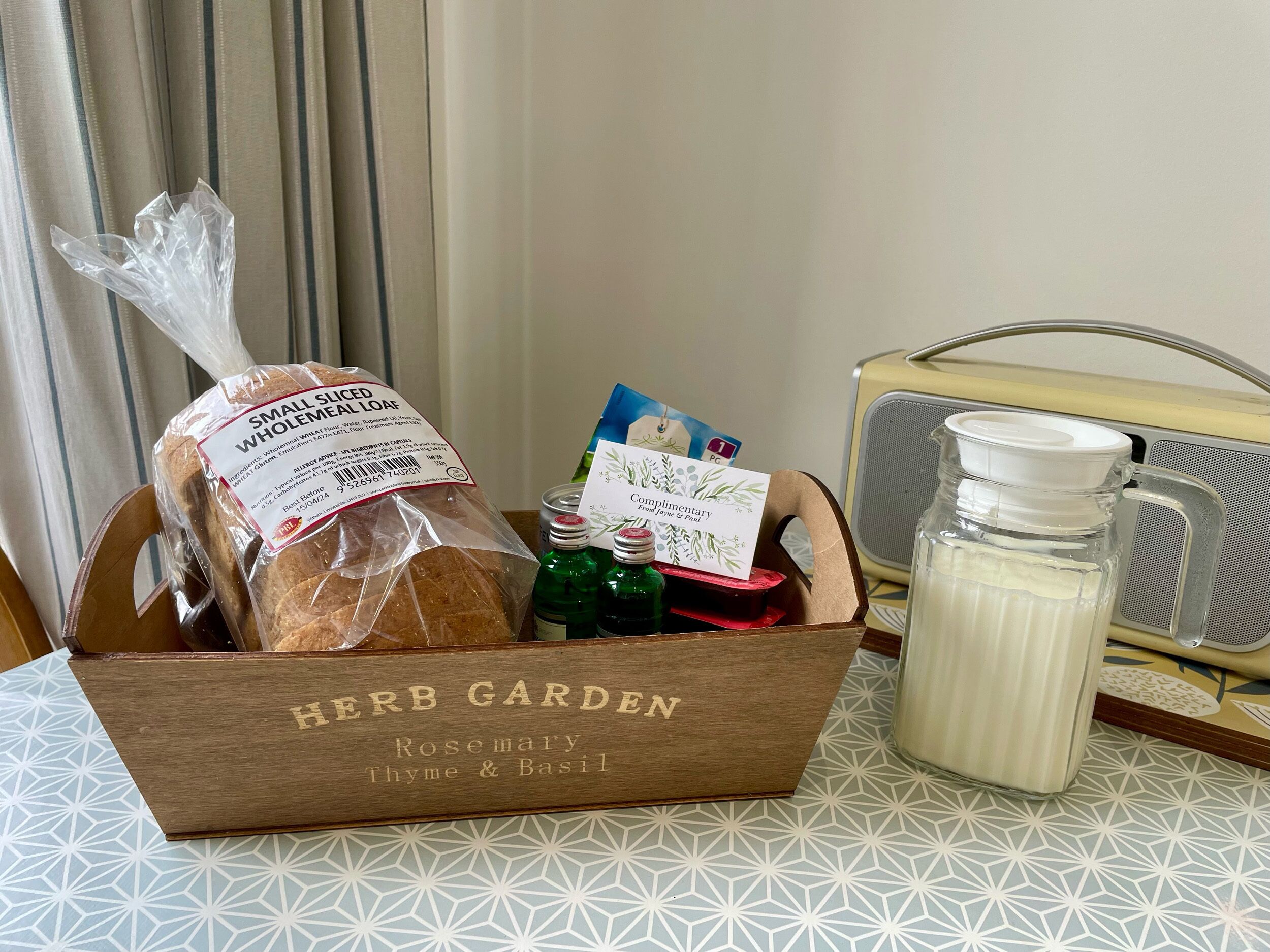 A wooden box labeled 'HERB GARDEN' with a loaf of bread, a card, and bottles on a table.