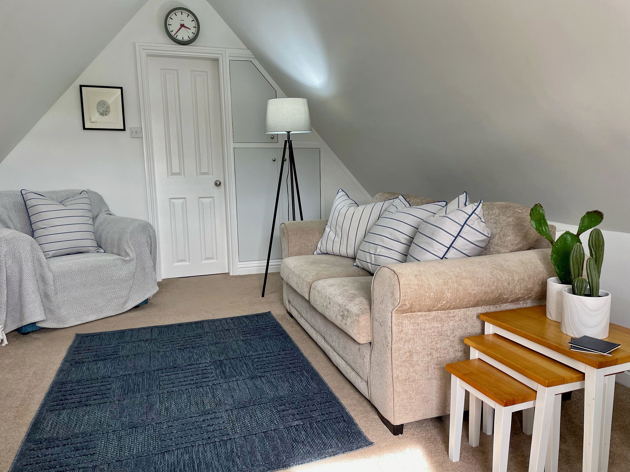 Un salon chaleureux avec un canapé beige, un fauteuil à motifs, un tapis bleu, une petite table en bois et un cactus en pot.