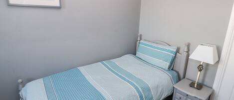 A bedroom with a single bed, a nightstand with a lamp, and a framed map on the wall.