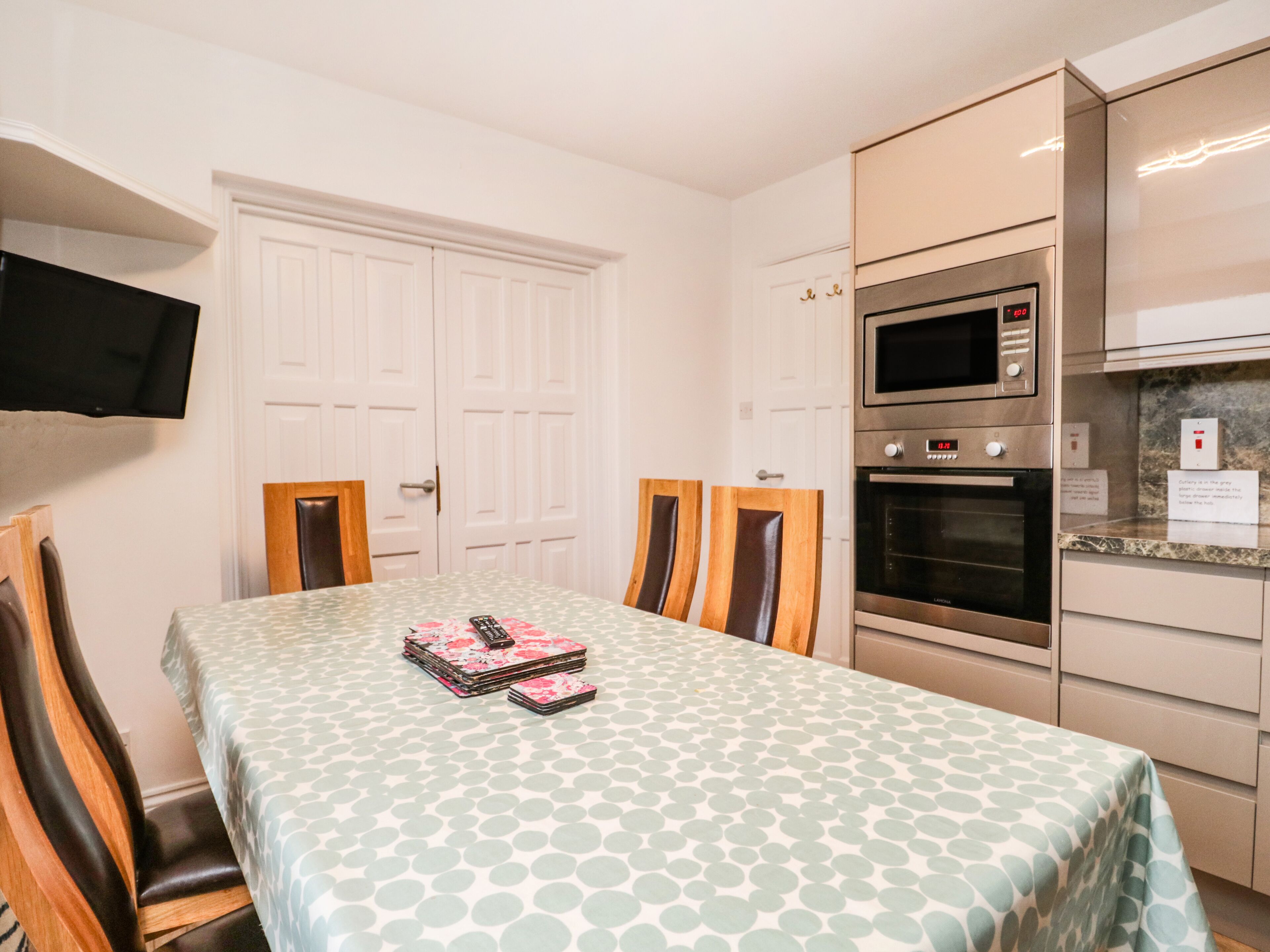 Een eethoek met een tafel gedekt voor vier personen, een magnetron, oven en een aan de muur bevestigde televisie.