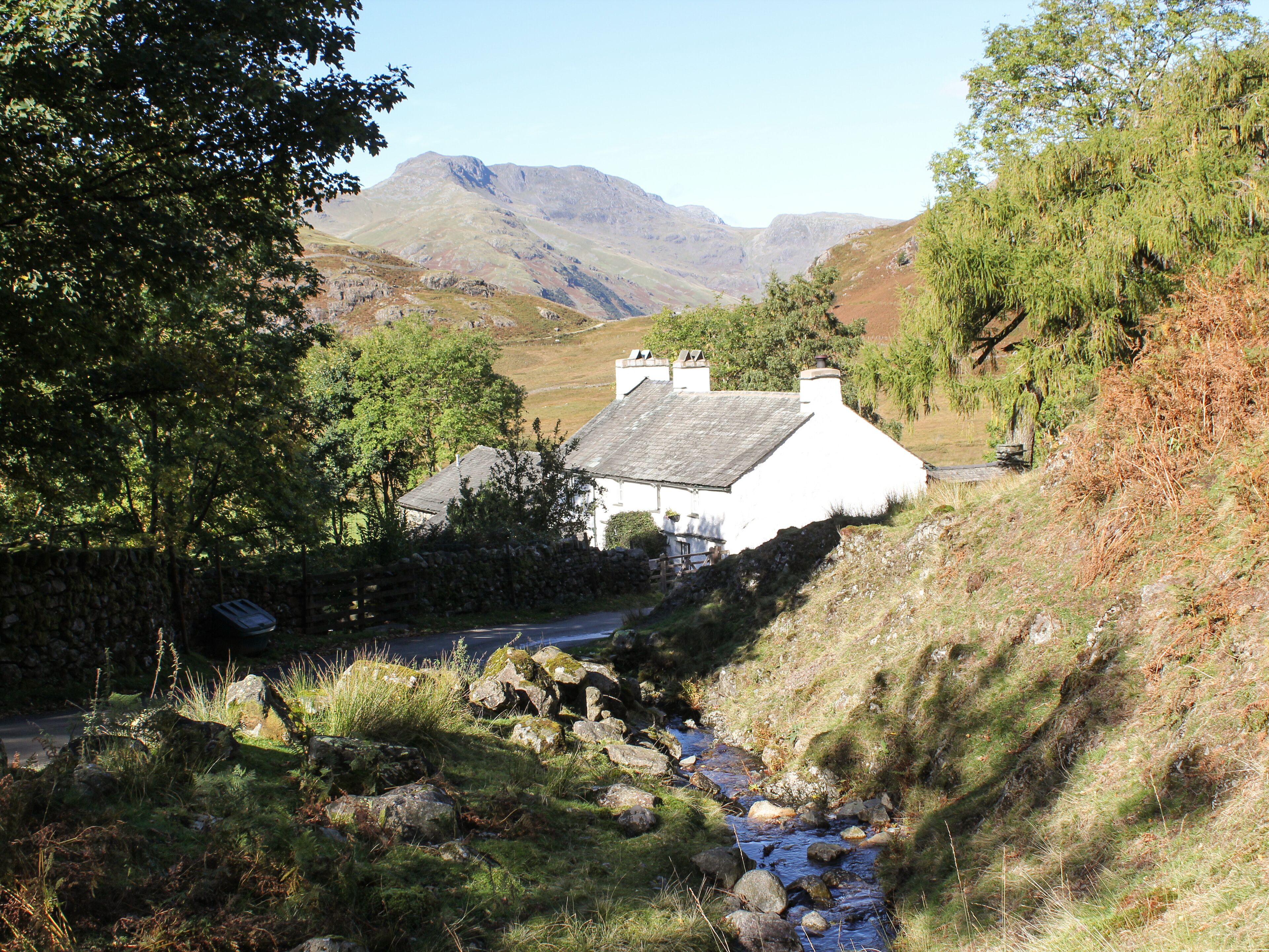A white house with a stone wall and a stream in front.