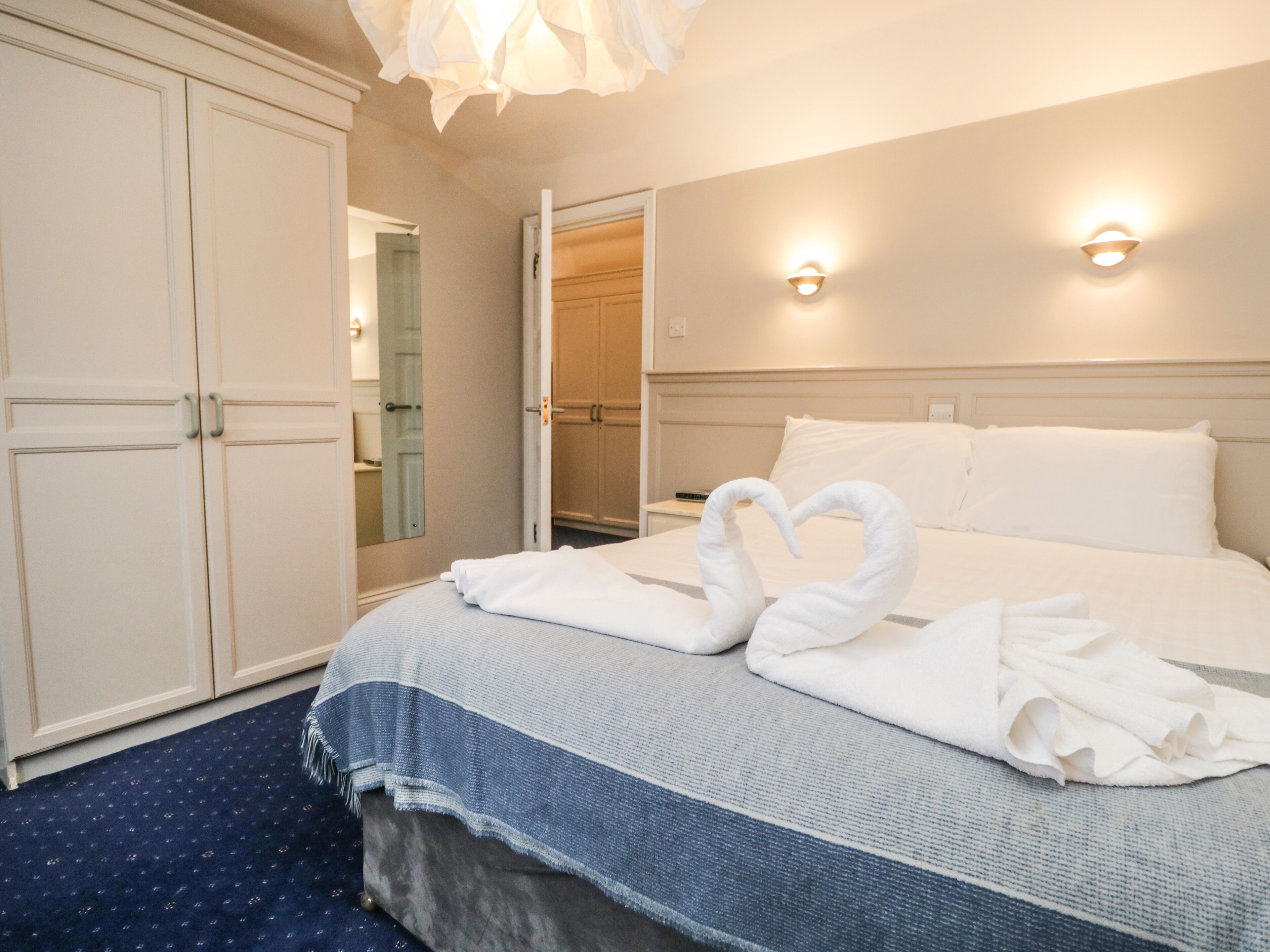 Quarto de hotel com cama, guarda-roupa, espelho e duas arandelas.