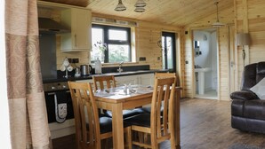 A wooden cabin interior with a dining table, chairs, a kitchen area, and a living room with a sofa. - Hayfields (King's Lynn)
