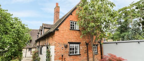 A traditional brick house with a stone pathway leading to a wooden table and chairs.