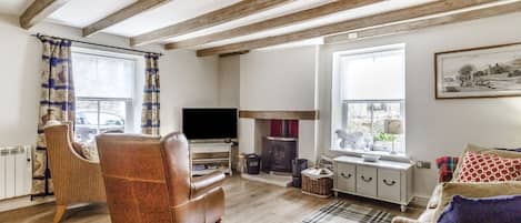 Ein gemütliches Wohnzimmer mit sichtbaren Holzbalken, einem Ledersessel, einem Fernseher und einem Kamin.