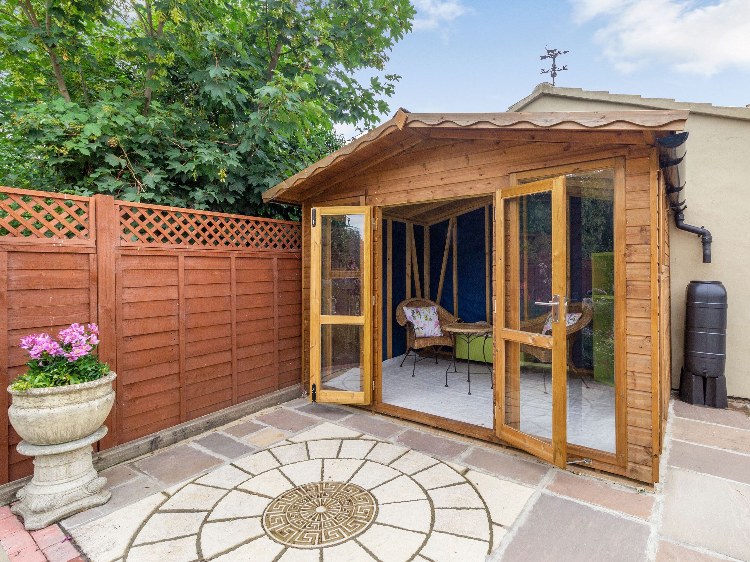A wooden gazebo with a glass door, a stone patio, and a wooden fence.
