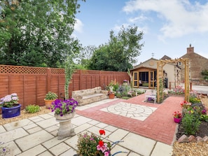 Une terrasse de jardin avec un sol en pierre, une pergola en bois et une variété de plantes et de fleurs en pot.