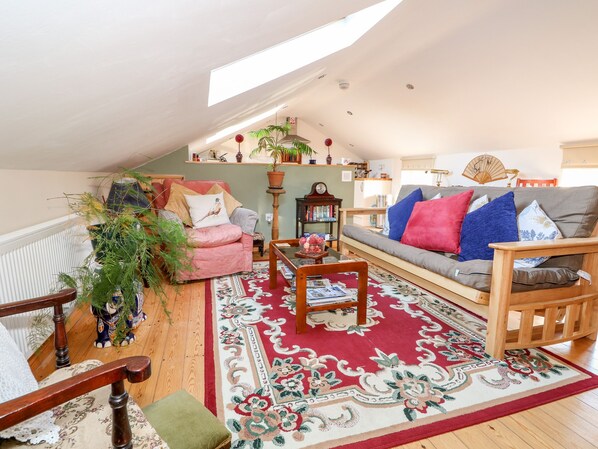 A cozy loft-style living room with a sloped ceiling, wooden furniture, a red patterned rug, and a variety of decorative items. - Berry Barn (Alford)