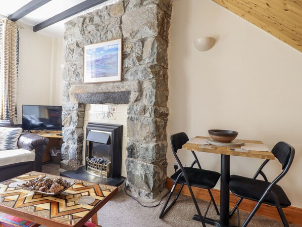 Een gezellige woonkamer met een stenen open haard, een televisie en een eethoek met stoelen en een tafel.