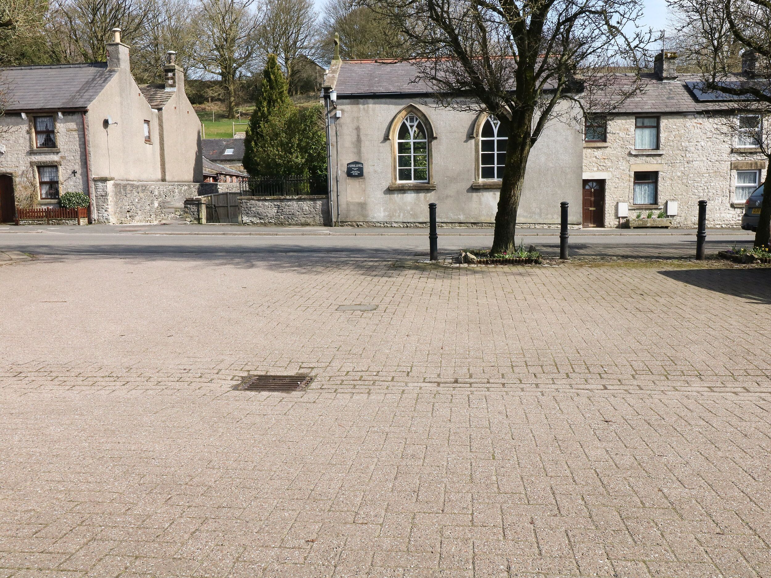 Une rue pavée bordée de bâtiments en pierre, dont une église aux arcs en ogive et un mur de pierre.