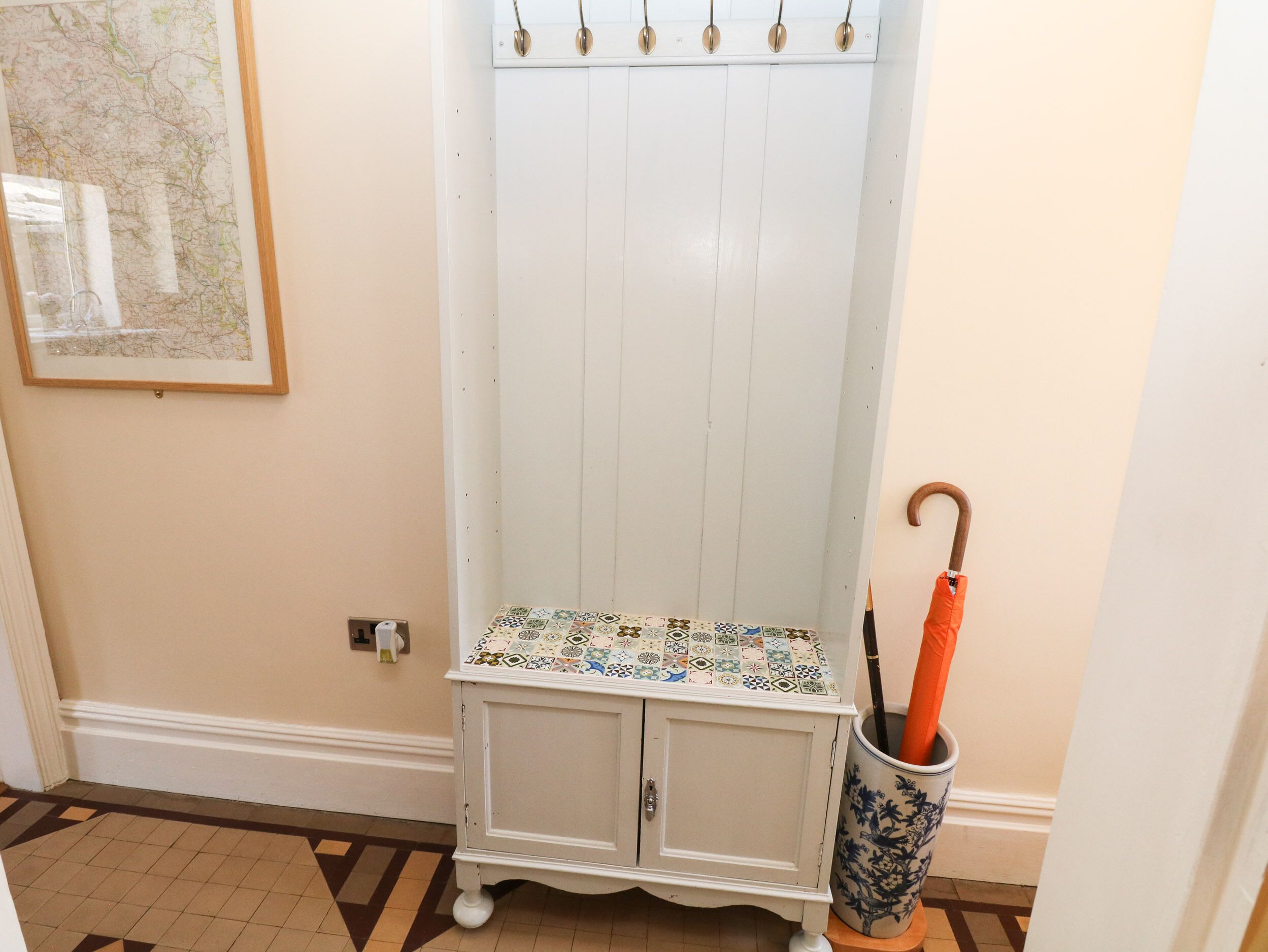 A corner with a white cabinet, a tiled bench, and a vase with an umbrella.