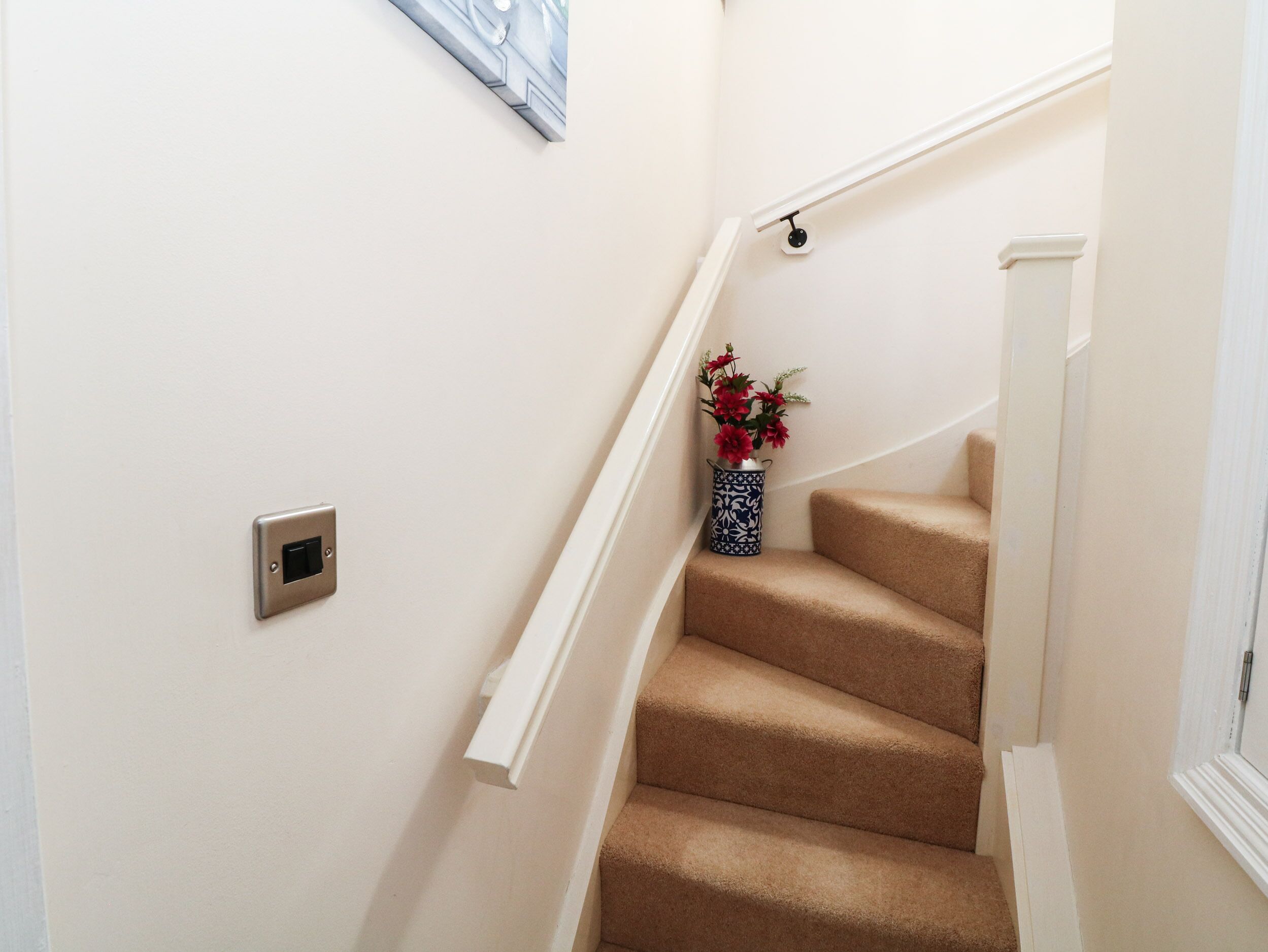 Un escalier recouvert de moquette, avec un interrupteur fixé au mur et un vase rempli de fleurs.