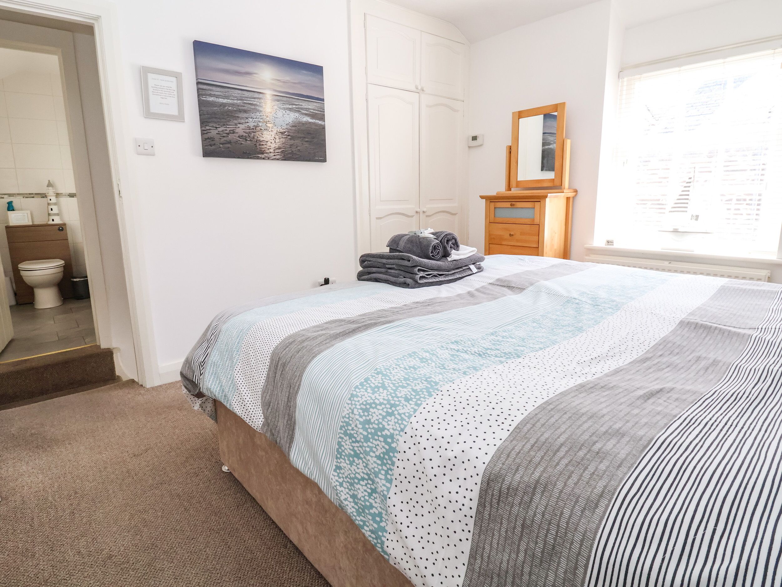 A bedroom with a bed, a bathroom with a toilet, and a window with blinds.