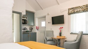A hotel room with a bed, a dining table with chairs, a kitchen area, and a TV mounted on the wall.