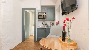A compact kitchen with a microwave, sink, and blue cabinets. A wooden table with a bottle and flowers is in the foreground.