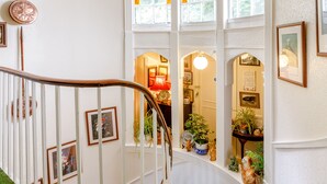 A staircase with white railings and a wooden handrail, leading to a landing with a view of a room with a red lamp and framed pictures. - Clooneavin Apartment 8 (Lynmouth)