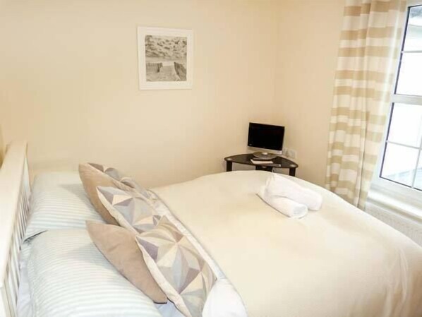 Habitación de hotel con cama, almohadas, mesita de noche con televisor y ventana con cortinas.