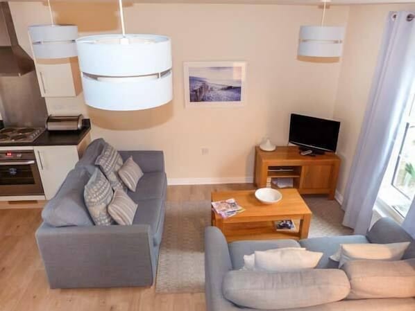 A modern living room with a grey sofa, a coffee table, and a TV on a wooden stand. - Hakuna Matata (Rye)