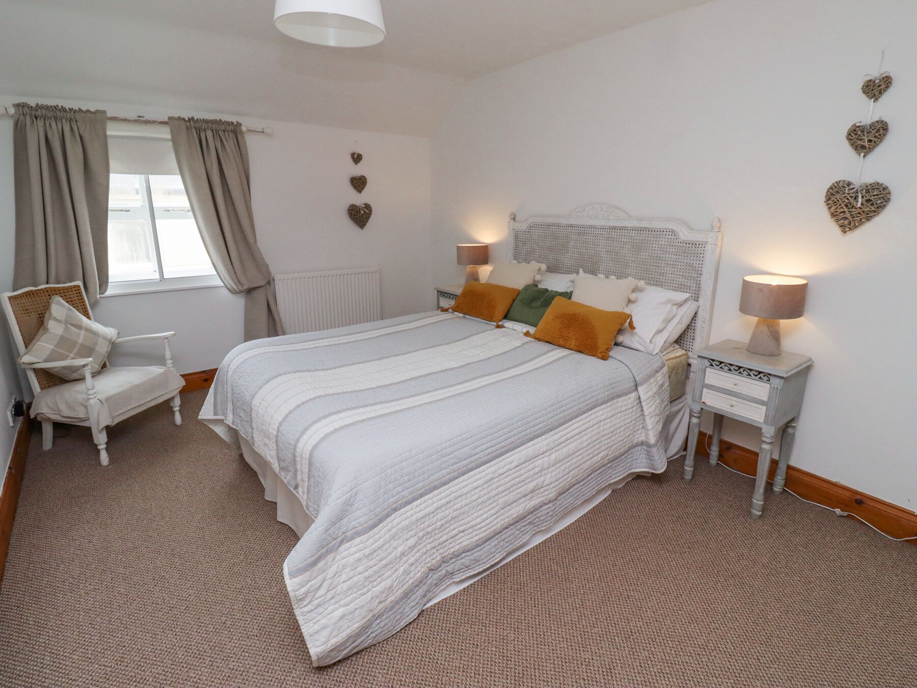 A bedroom with a bed, a chair, a nightstand, and decorative heart wall art.
