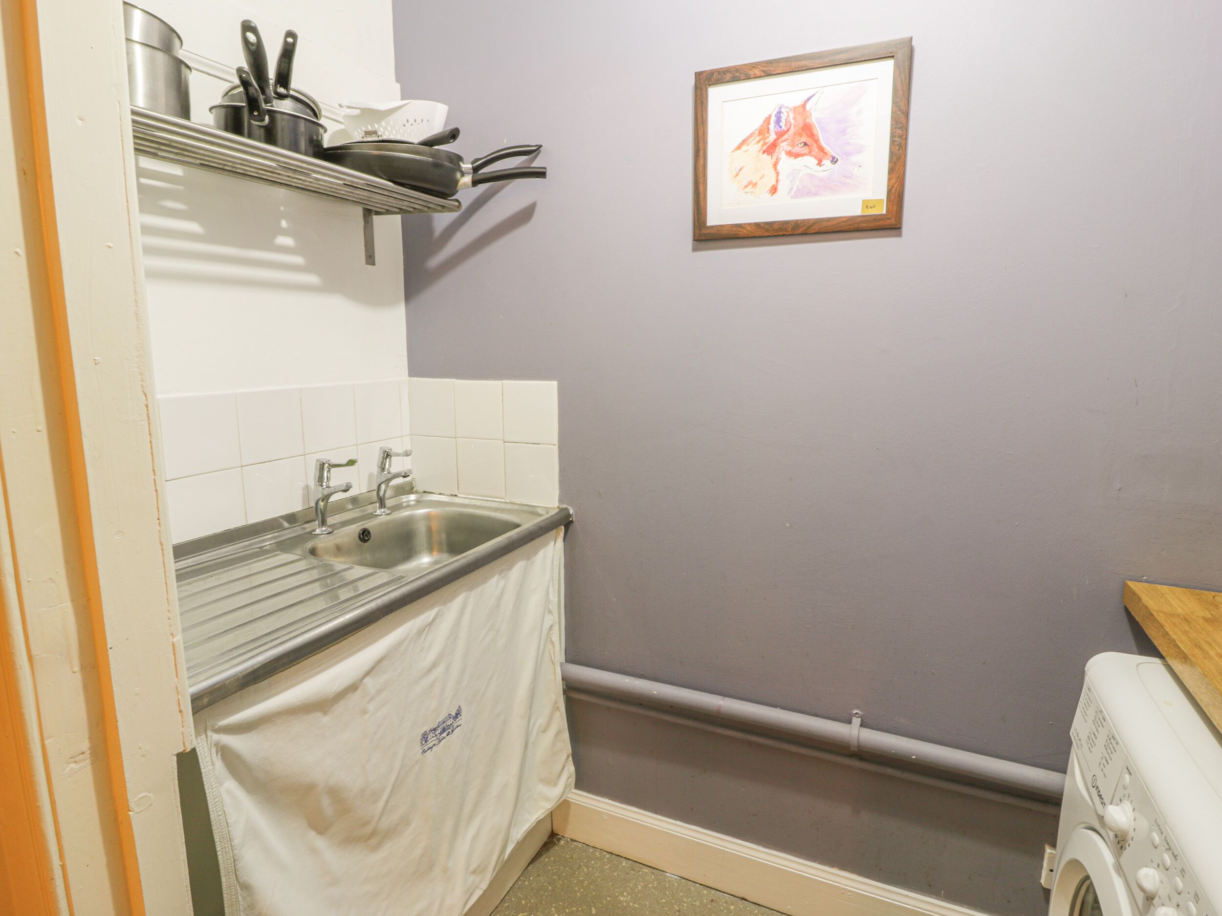 A kitchen with a sink, a stove, and a shelf above the sink holding pots and pans.