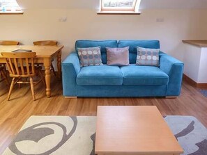 A living room with a blue sofa, wooden chairs, a wooden coffee table, and a patterned rug. - Lakefield Apartment (Inverness)